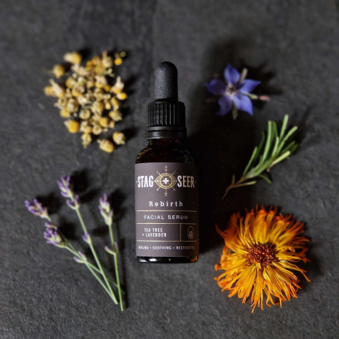Face serum bottle surrounded by flowers and herbs on slate background